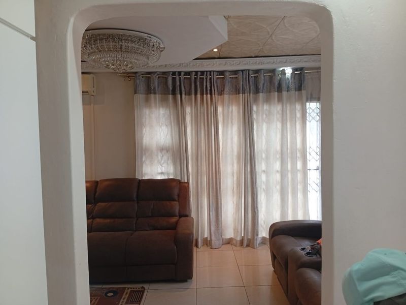A living room featuring an arched entryway, tiled flooring, decorative ceiling tiles, and a crystal chandelier, providing a classic aesthetic.