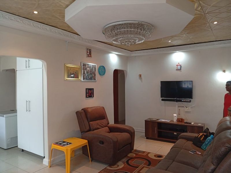 A living room featuring decorative ceiling tiles, a central crystal chandelier, and tiled flooring, with an archway leading to adjacent living spaces.