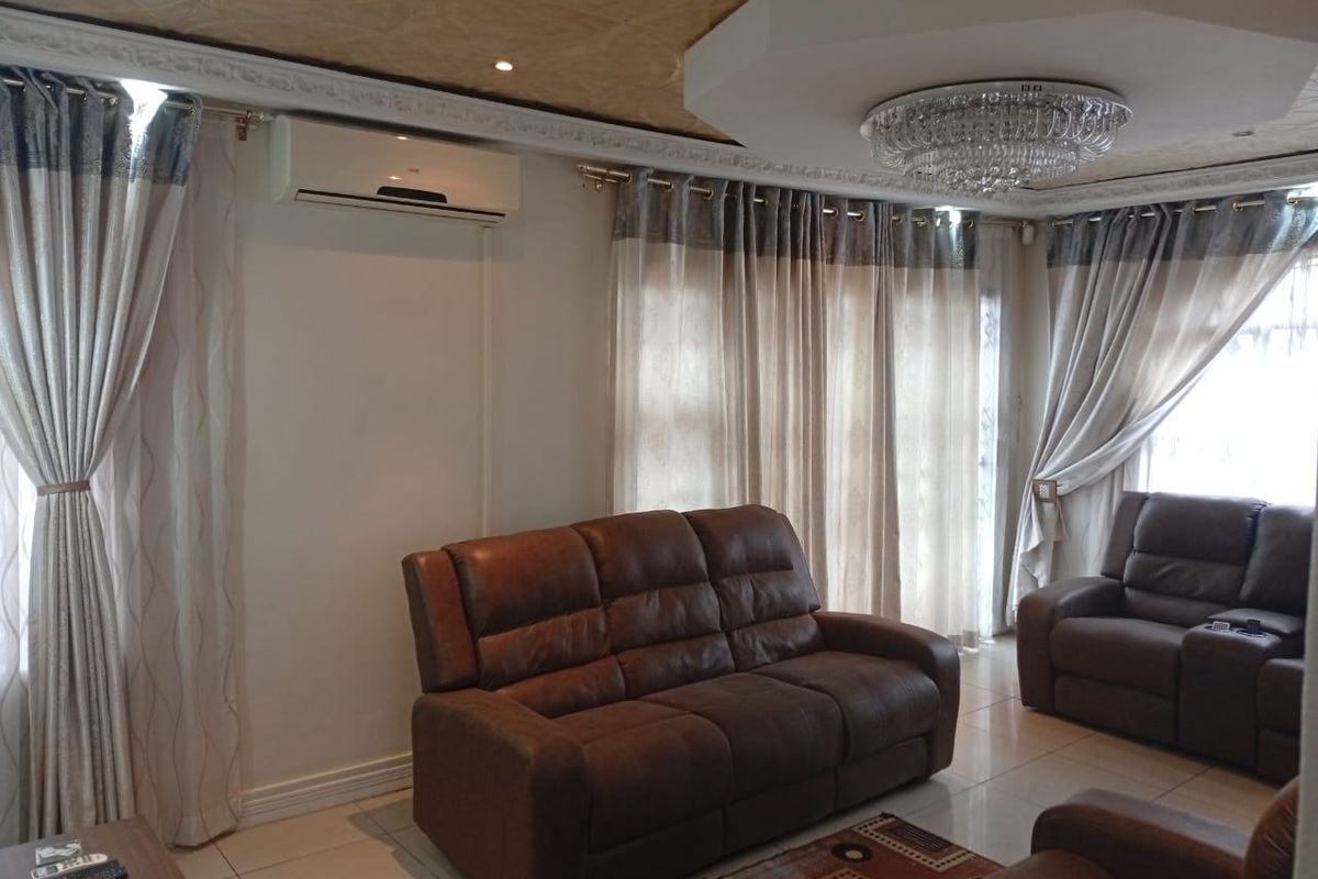 A well-maintained living room featuring tiled flooring, decorative ceiling detailing, and a wall-mounted split-system air conditioner.