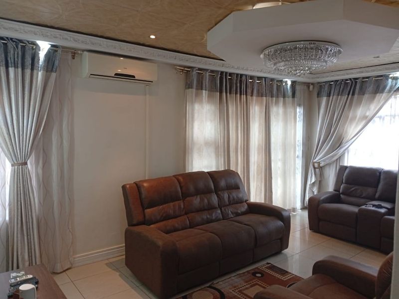 A well-maintained living room featuring tiled flooring, decorative ceiling detailing, and a wall-mounted split-system air conditioner.