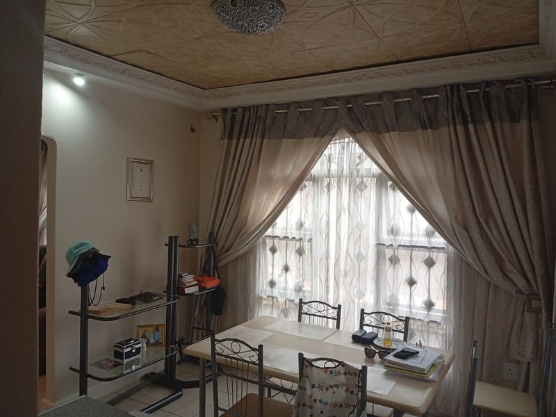 A dining room featuring decorative ceiling tiles, crown molding, and a large window with curtains, providing a functional space for meals.