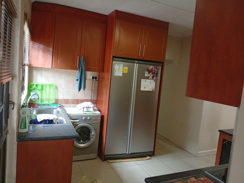 A functional kitchen featuring wooden cabinetry, granite countertops, a stainless steel sink, and tiled flooring with space for integrated appliances.
