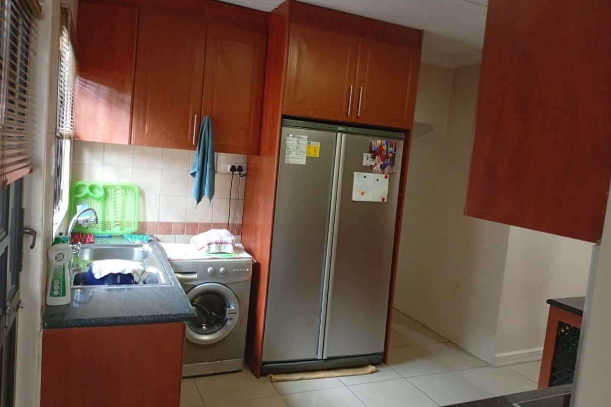 A functional kitchen featuring wooden cabinetry, granite countertops, a stainless steel sink, and tiled flooring with space for integrated appliances.