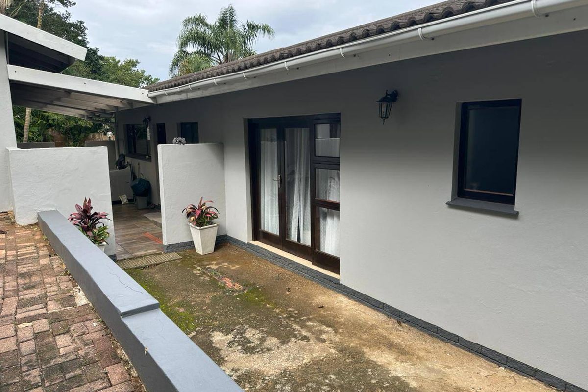 Rear exterior view featuring a paved patio area, sliding glass doors, and a low brick retaining wall with neutral grey exterior finishes.