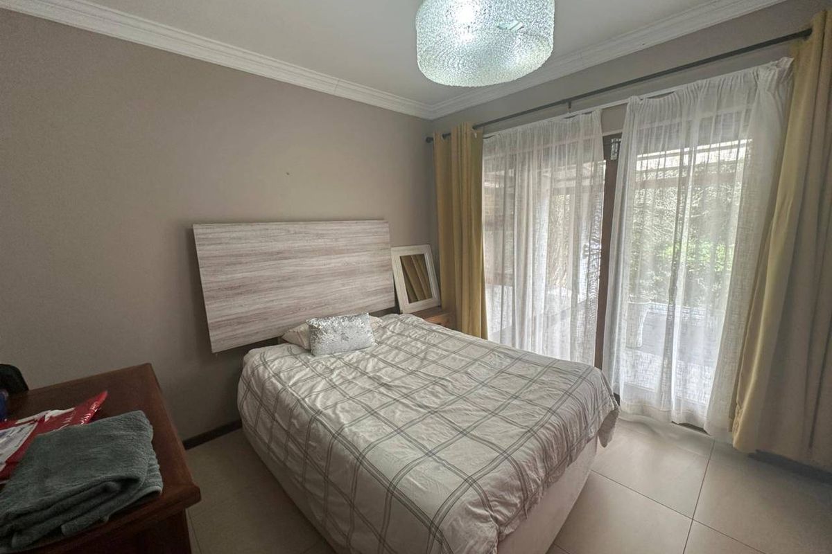 A well-lit bedroom featuring neutral tiled flooring, crown molding, and a large sliding glass door providing access to the exterior.