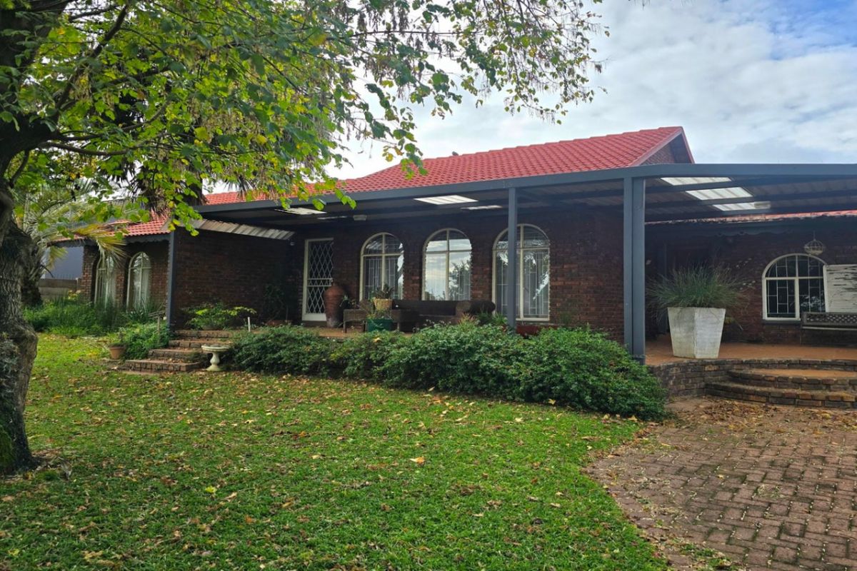 Rear view of a brick house featuring a covered patio, arched windows, and a well-maintained garden with mature trees.