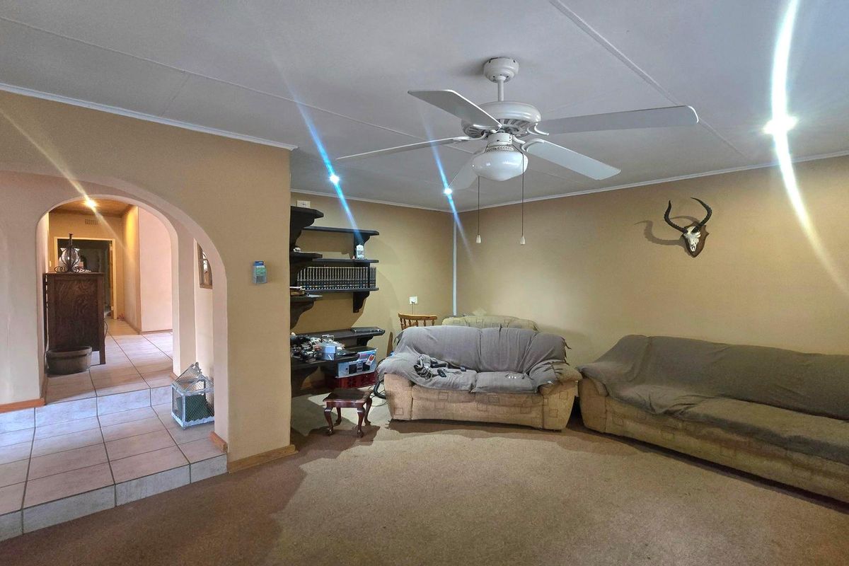 A living room featuring a ceiling fan, carpeted flooring, and an arched entryway leading to a tiled hallway with built-in shelving.