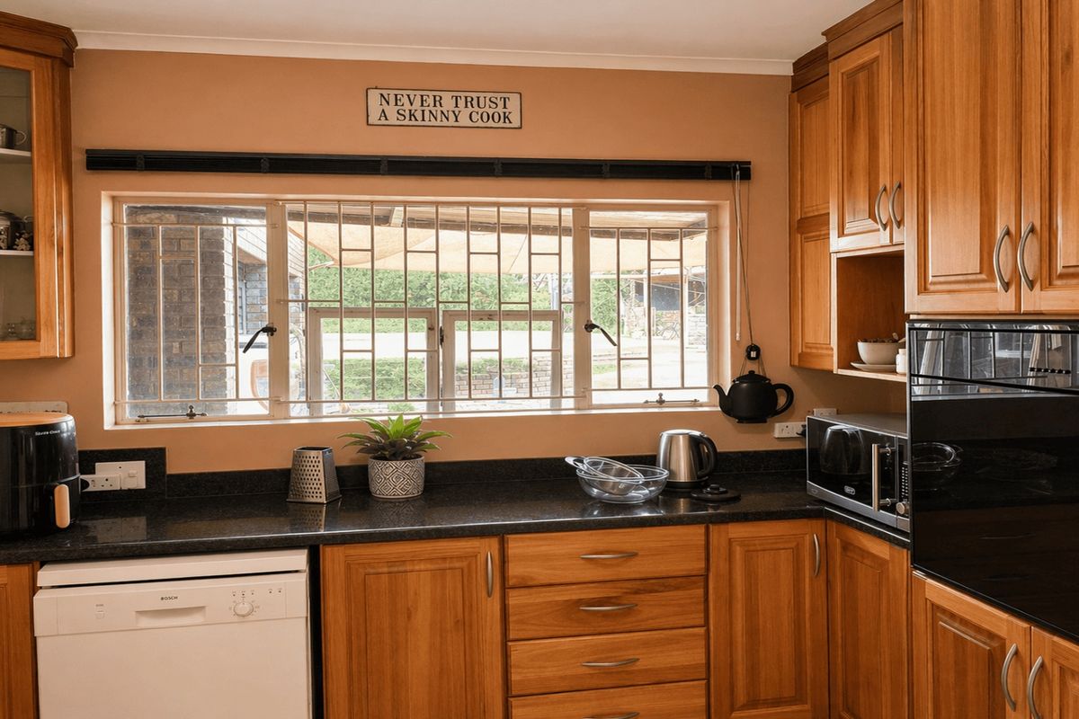 A functional kitchen featuring warm-toned wooden cabinetry, dark granite countertops, built-in oven, and a window with security bars overlooking the exterior.