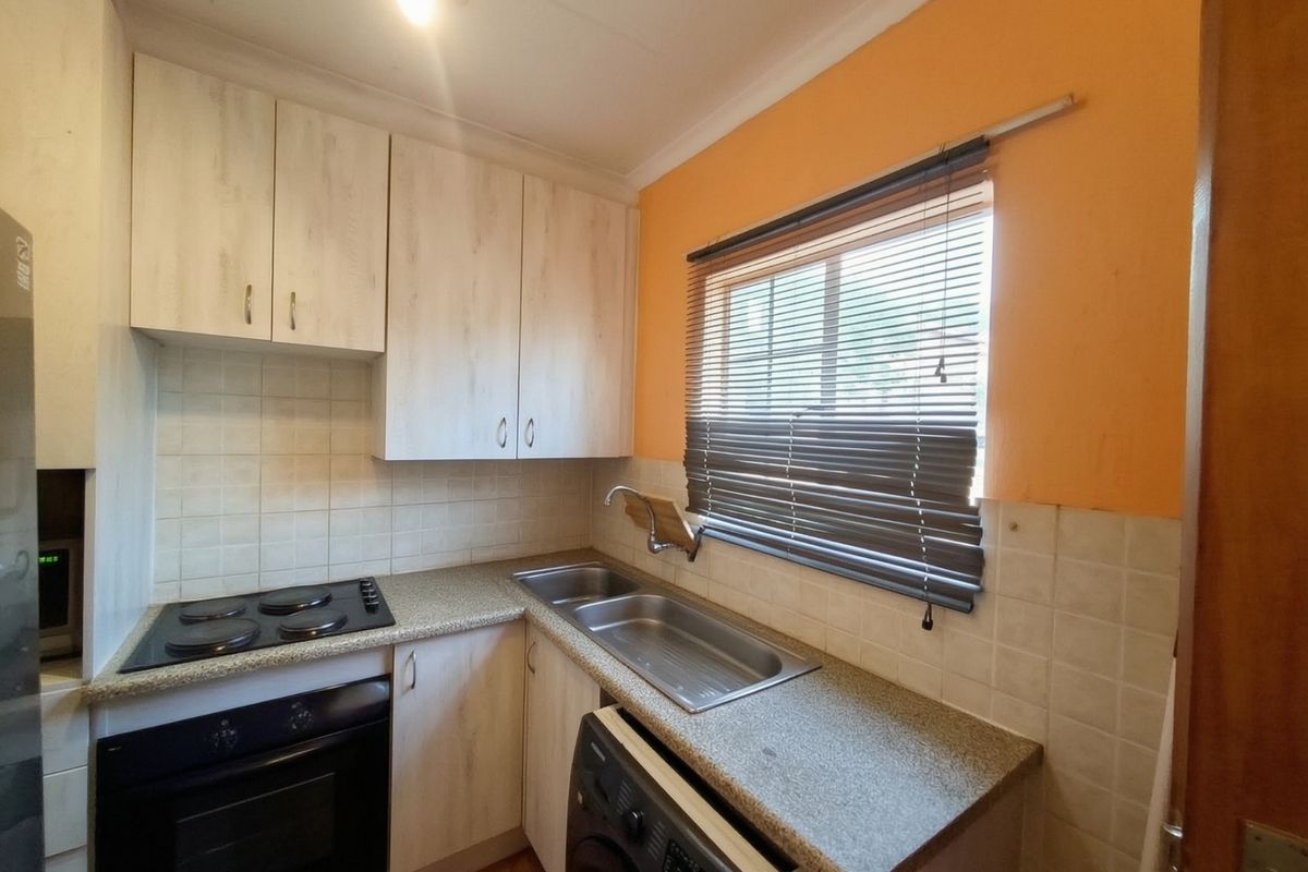 Compact kitchen featuring light wood-look cabinetry, laminate countertops, a double stainless steel sink, and built-in electric cooking appliances.