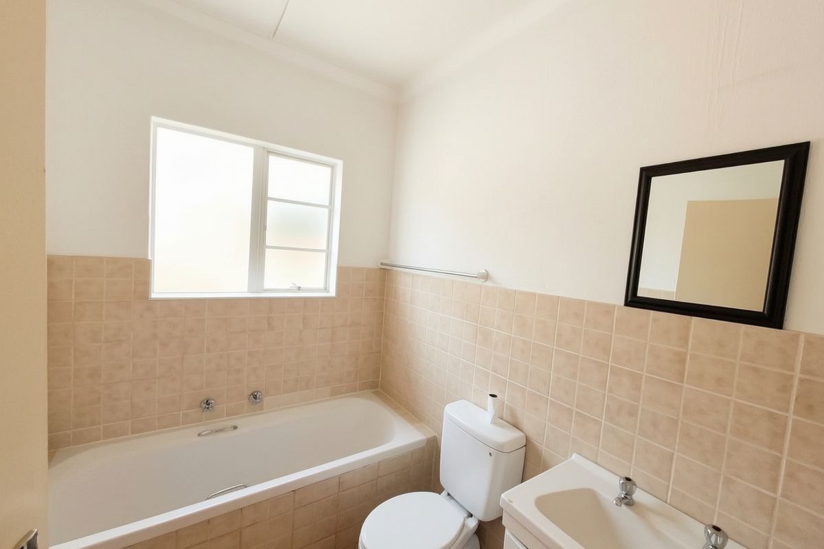 A functional bathroom featuring a bathtub, toilet, and vanity basin with neutral wall tiling and natural light from a frosted window.