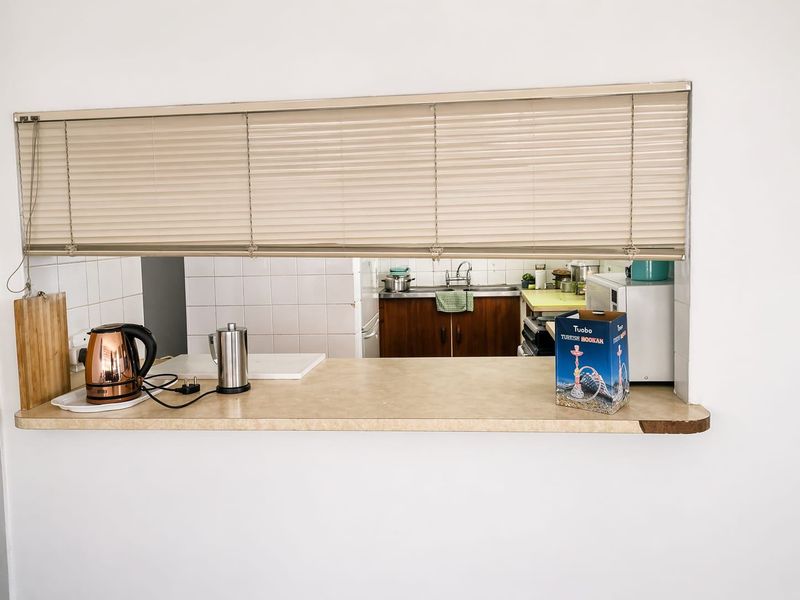 A kitchen serving hatch featuring a laminate countertop, built-in cabinetry, and a stainless steel sink, providing a functional connection between living and cooking areas.