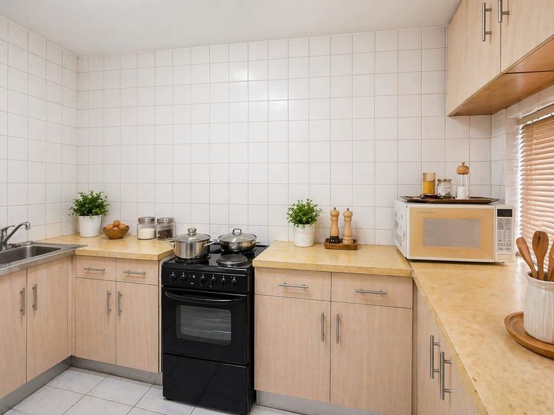 A functional kitchen featuring light wood-finish cabinetry, laminate countertops, a tiled backsplash, and a freestanding black oven.