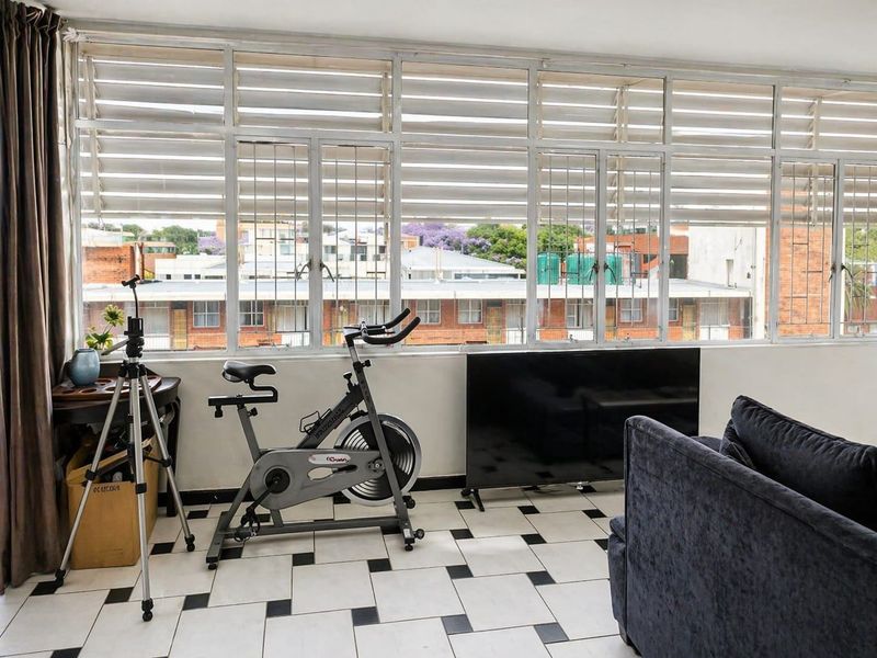 A living area featuring large windows with security bars, black and white tiled flooring, and an urban neighborhood view.