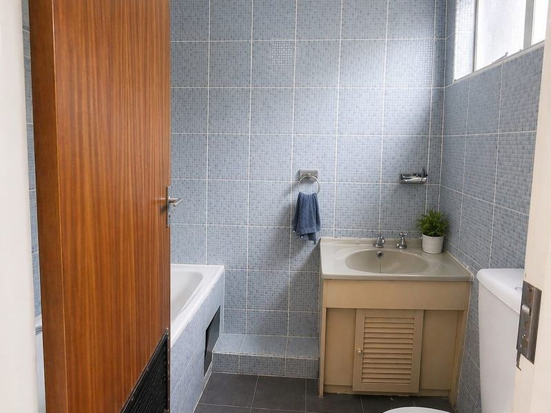A functional bathroom featuring blue wall tiling, a built-in bathtub, a vanity basin, and a toilet.