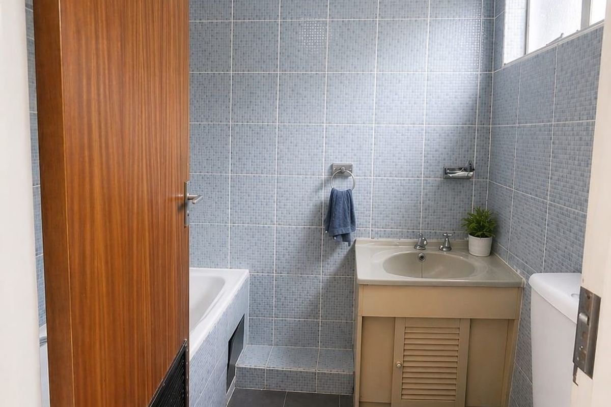 A functional bathroom featuring blue wall tiling, a built-in bathtub, a vanity basin, and a toilet.