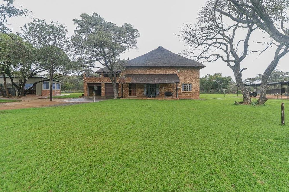 A spacious rear view of a face brick farmhouse featuring a traditional thatched roof, a covered patio, and an expansive surrounding lawn.