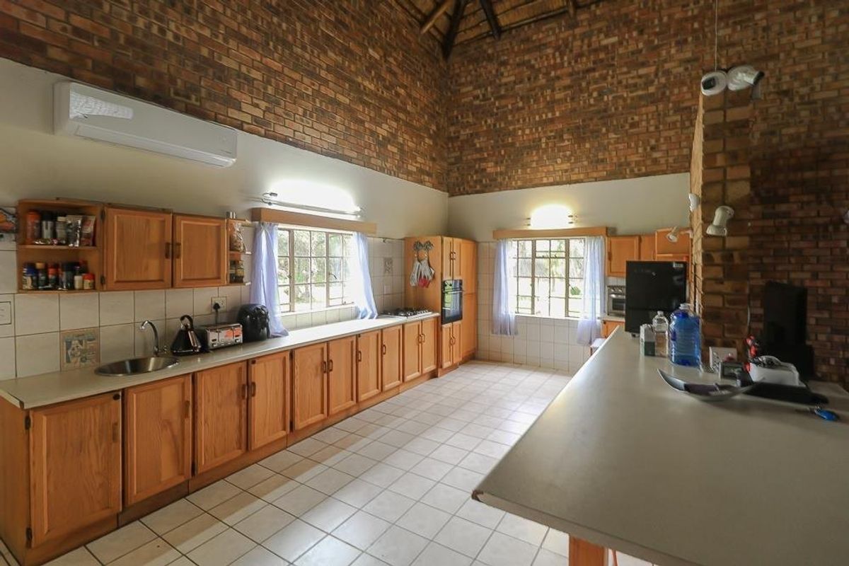 Spacious farmhouse kitchen featuring exposed brick walls, a high vaulted thatched ceiling, wooden cabinetry, tiled flooring, and a functional breakfast counter.