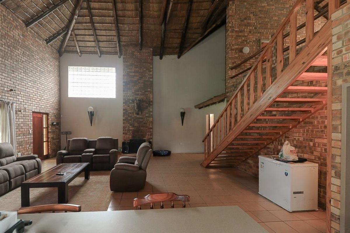 Spacious living area featuring high vaulted ceilings with exposed thatch and timber rafters, facebrick walls, a fireplace, and a timber staircase.