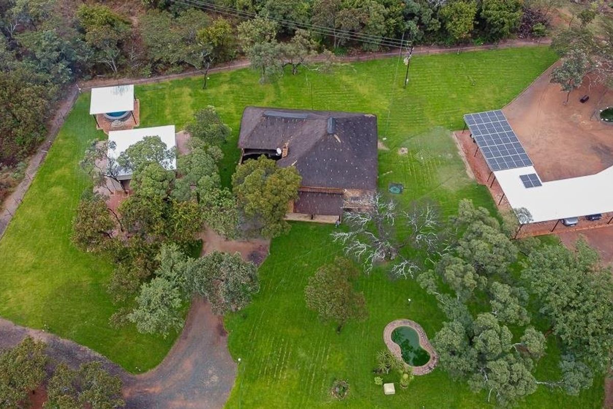 Aerial view of a farm property featuring a thatched-roof main house, outbuildings, a swimming pool, and a large carport with solar panels.