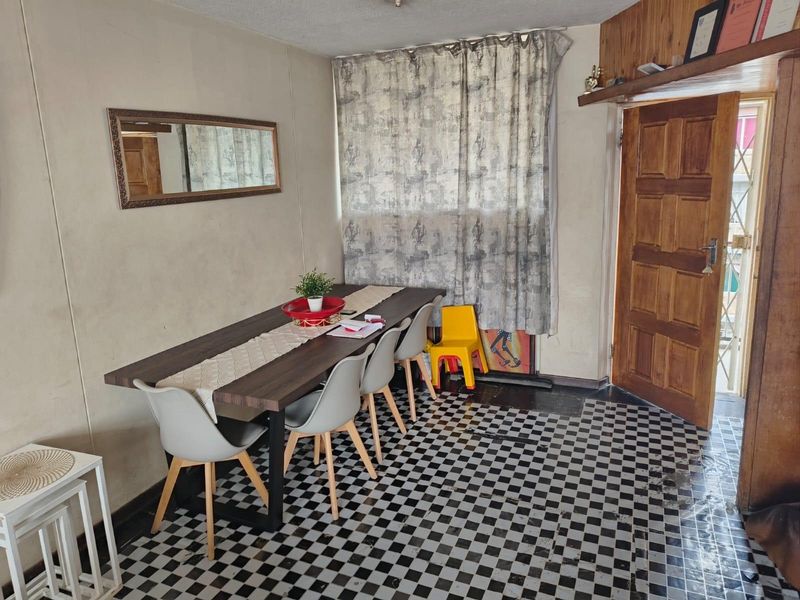 Dining area featuring a distinctive checkered tile floor, timber door, and wood paneling accents, offering a functional space with potential for cosmetic updates.