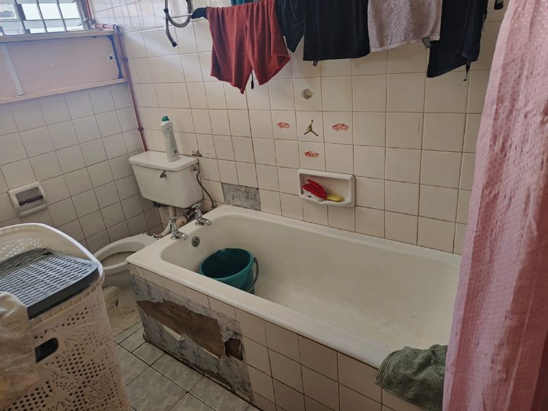 A dated bathroom featuring a bathtub and toilet, currently requiring repairs to the bathtub paneling and wall tiling.