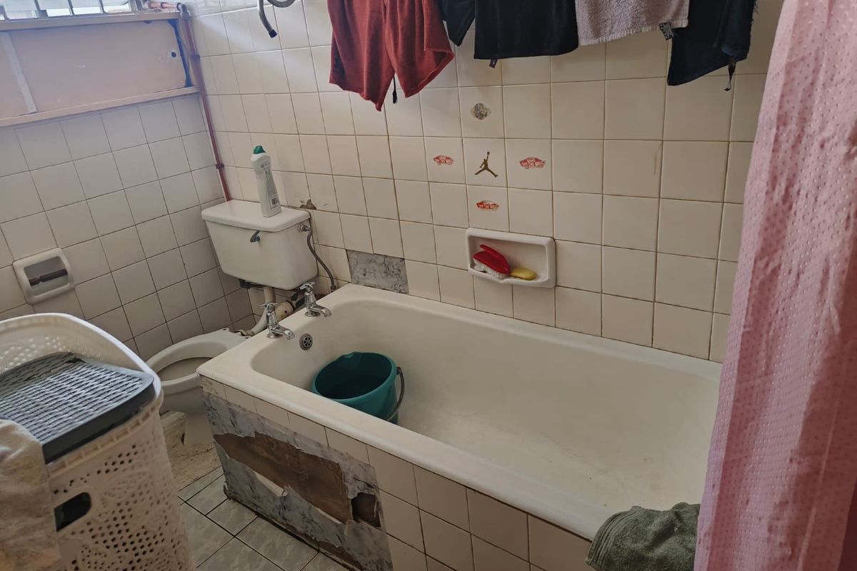 A dated bathroom featuring a bathtub and toilet, currently requiring repairs to the bathtub paneling and wall tiling.