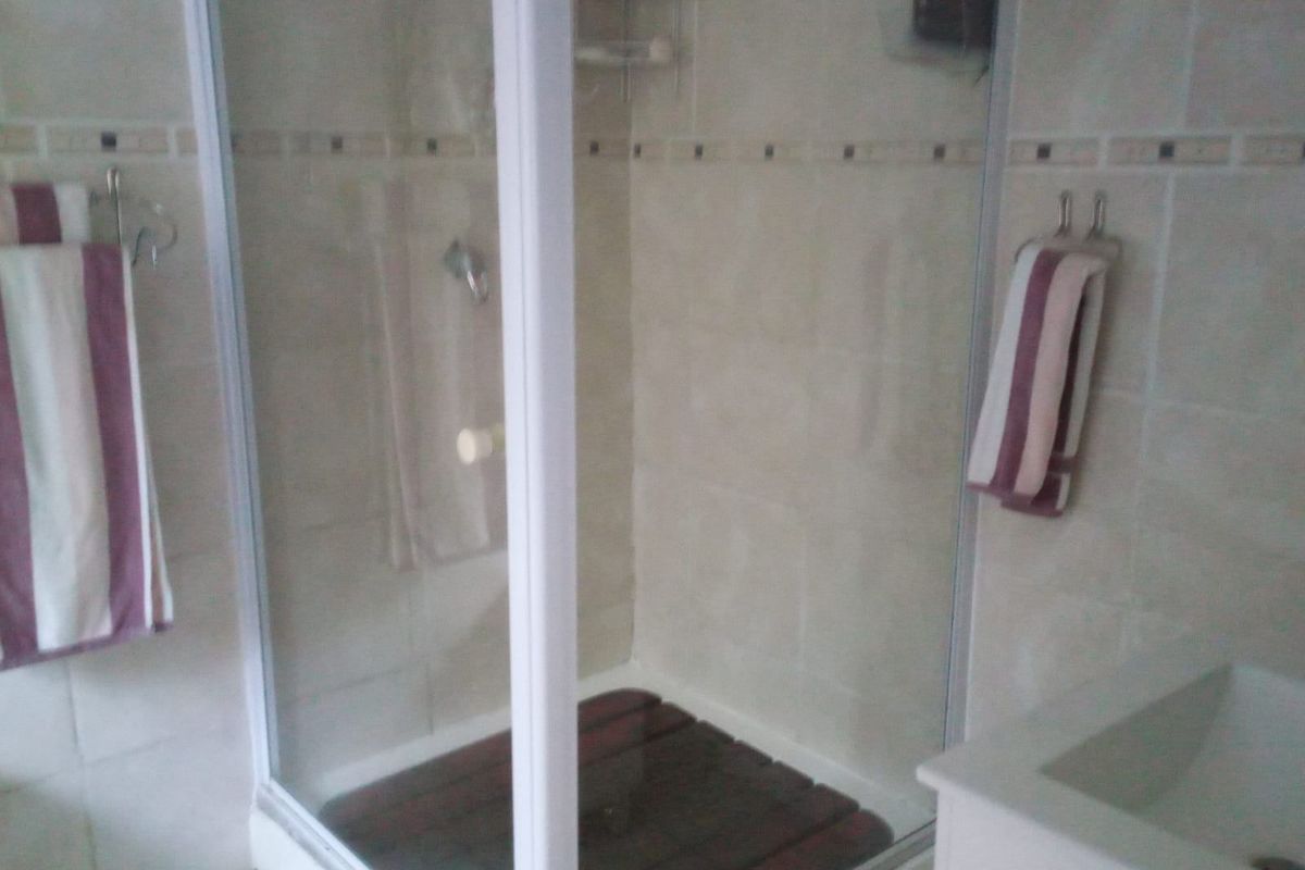 A functional bathroom featuring a glass-enclosed shower with tiled walls and a vanity basin.