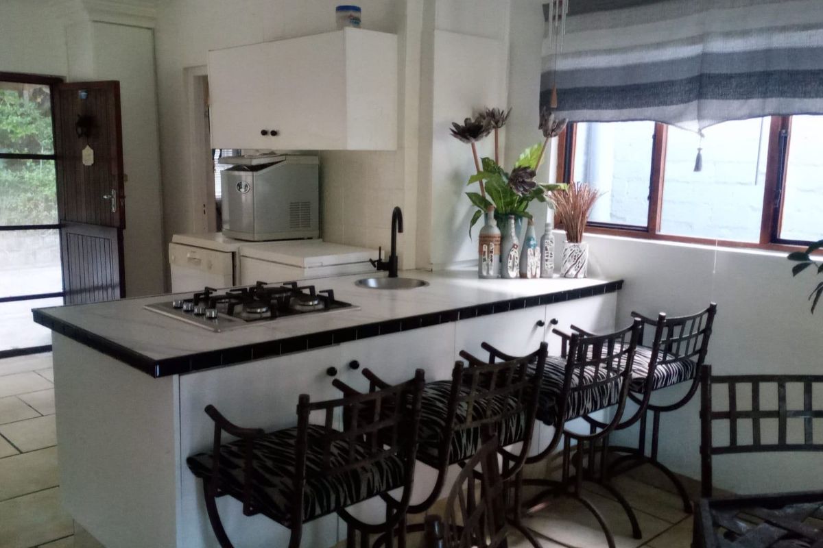 A functional kitchen featuring a central island with a built-in gas hob, tiled countertops, and ample cabinetry, offering a practical layout for cooking and dining.
