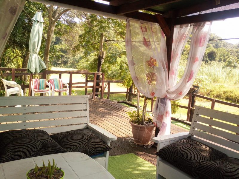 A covered timber deck patio featuring wooden railings and a pergola structure, overlooking a natural garden setting.