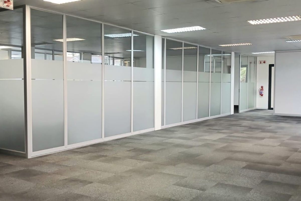 Open plan commercial office space featuring glass partition walls, suspended ceilings with recessed lighting, and durable carpet tiles.