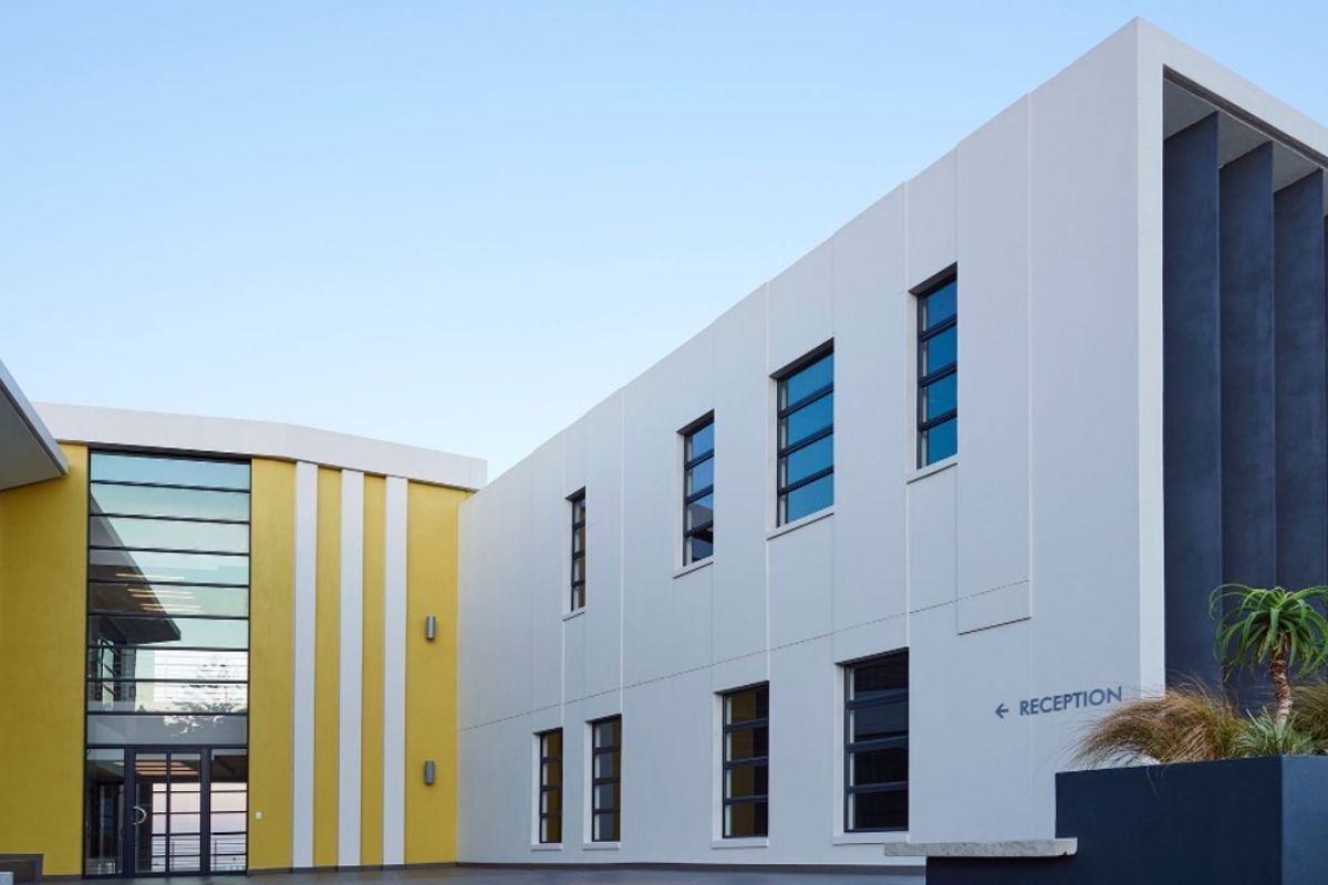 Modern commercial building facade featuring a striking yellow accent wall, large glass entrance, and clean white architectural lines with clear reception signage.