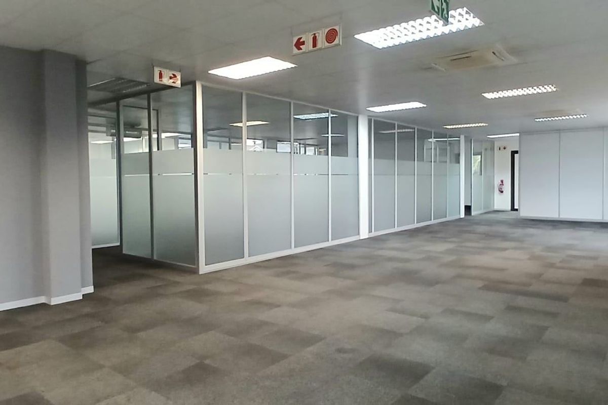 Spacious open-plan commercial office area featuring glass partitioning, carpet tiles, suspended ceilings with recessed lighting, and integrated air conditioning.