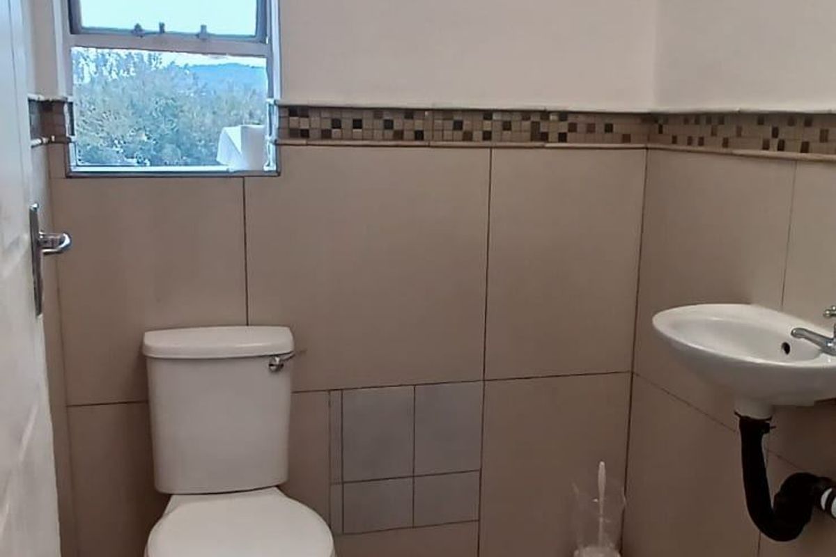 A functional bathroom featuring ceramic floor and wall tiling, a standard toilet, and a pedestal basin with exposed plumbing.