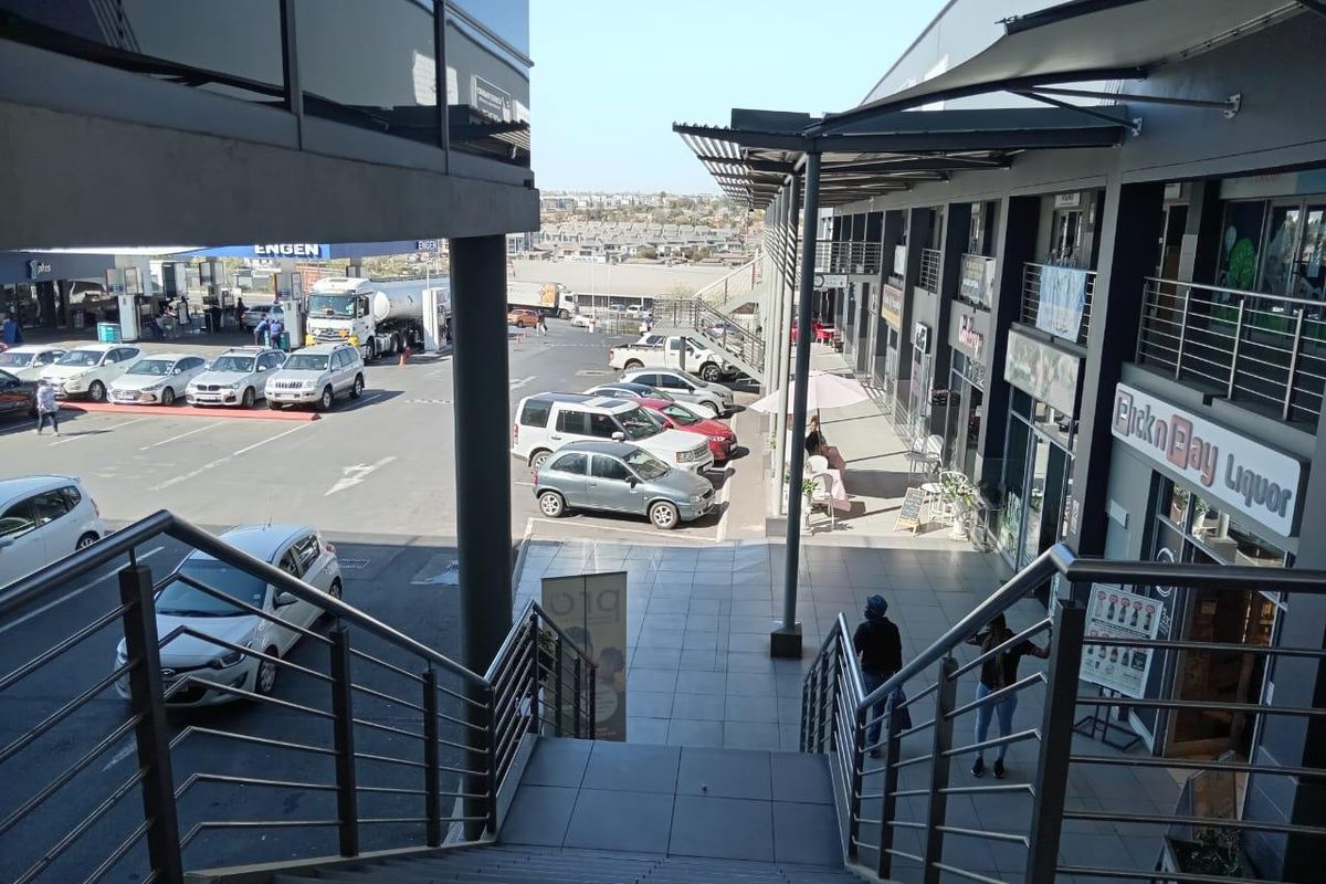 View from an elevated staircase overlooking a commercial parking area and retail storefronts with modern glass and metal architectural finishes.