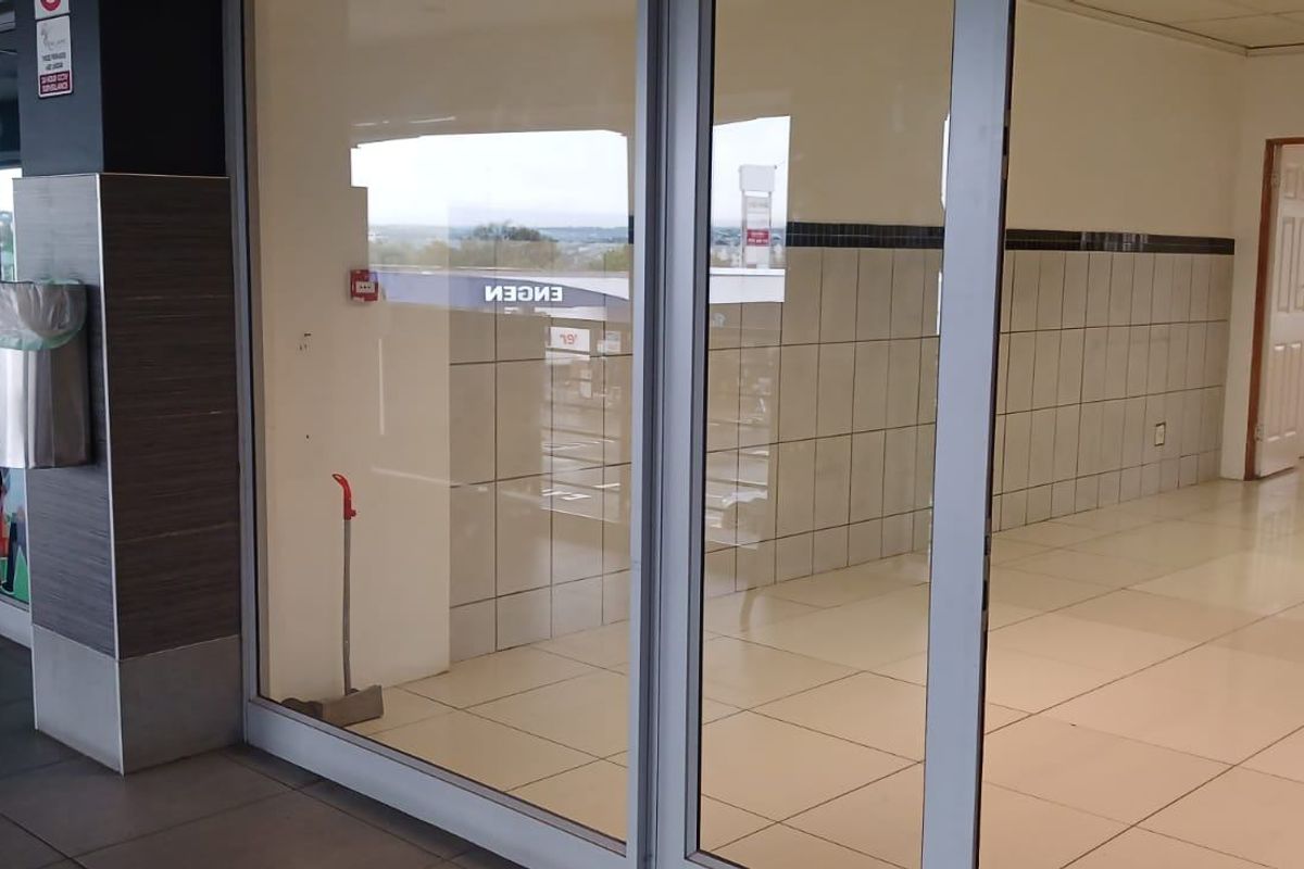 Empty commercial office space featuring tiled flooring, glass storefront entrance, and tiled wall accents, suitable for retail or professional use.