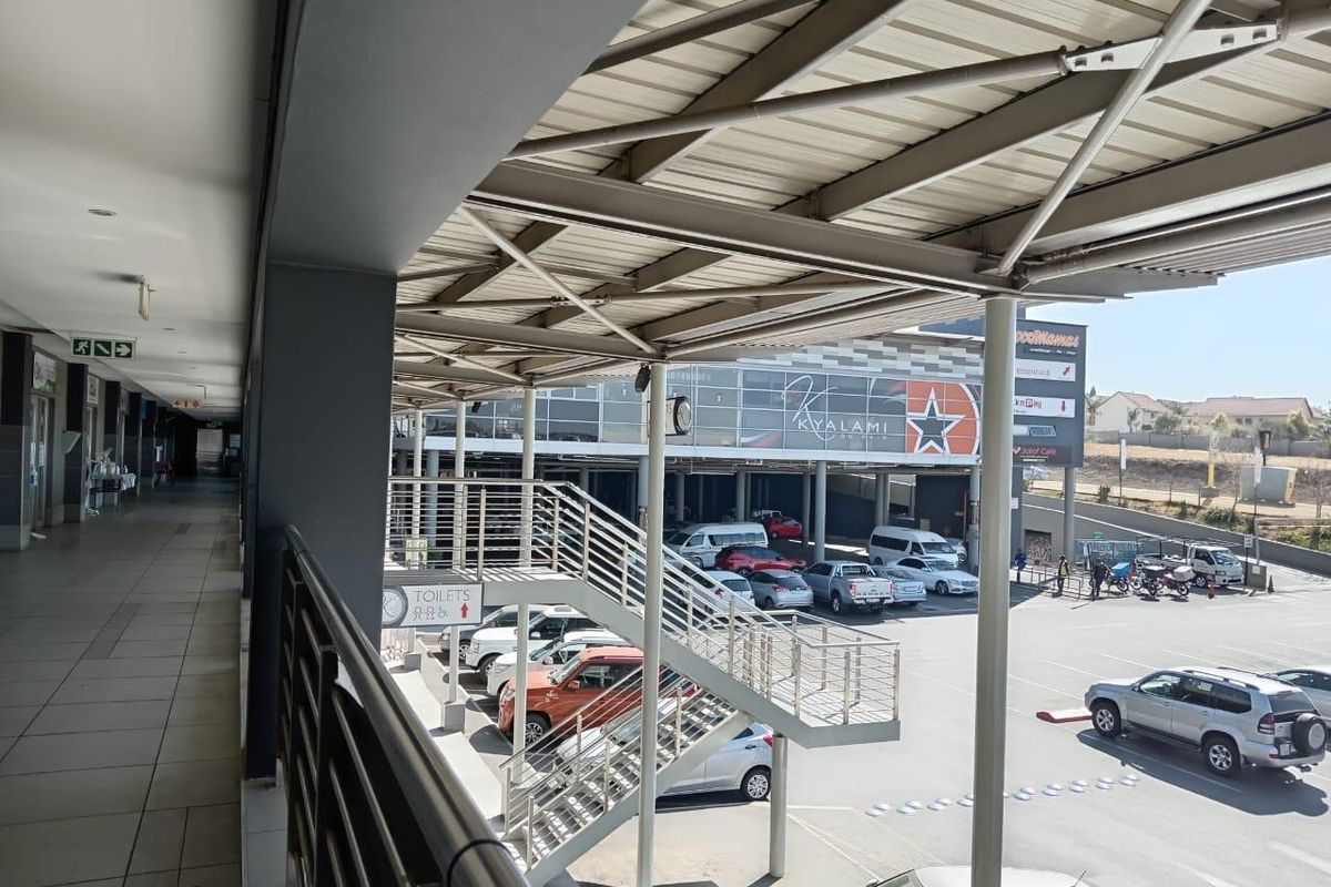 An elevated view of a commercial property exterior featuring a covered walkway, steel staircase, and parking area with signage.