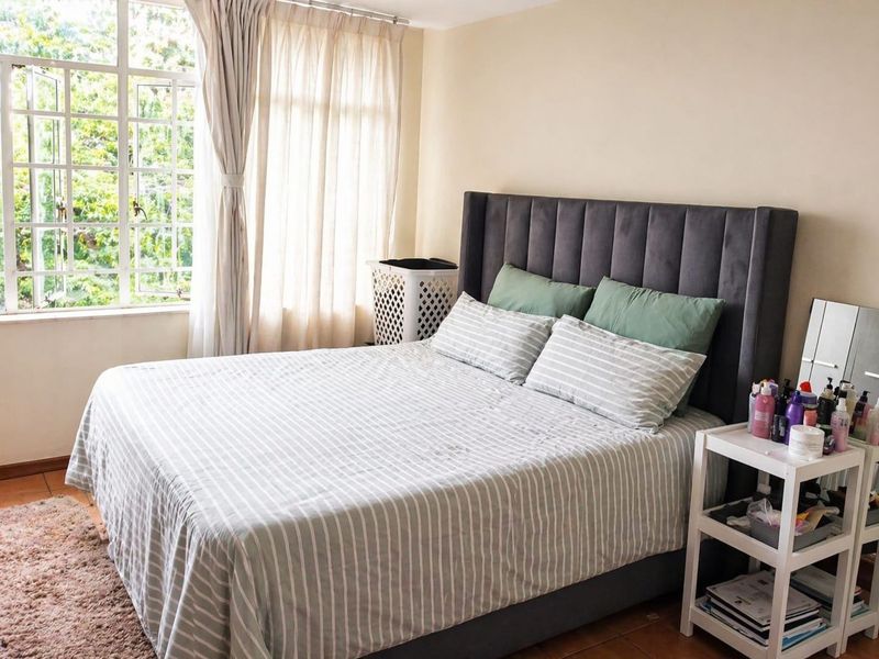 A well-lit bedroom featuring large windows with natural light, tiled flooring, and neutral wall finishes.