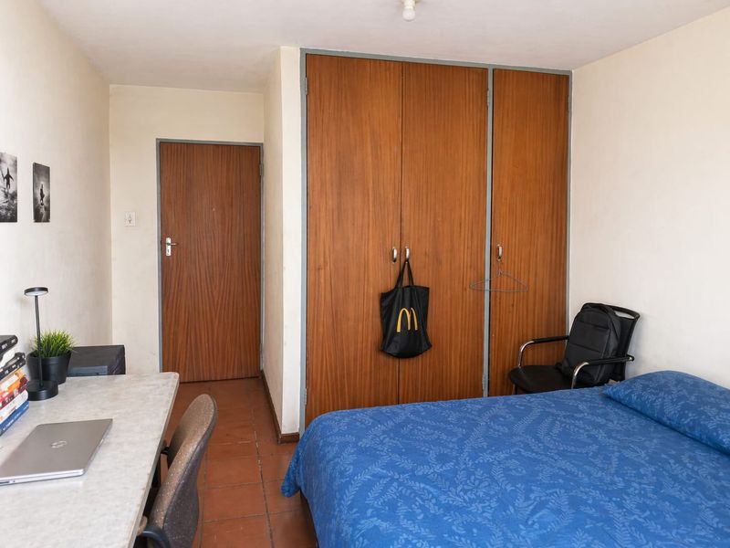 A functional bedroom featuring built-in wooden wardrobes, tiled flooring, and a standard internal door, offering a practical layout for living.