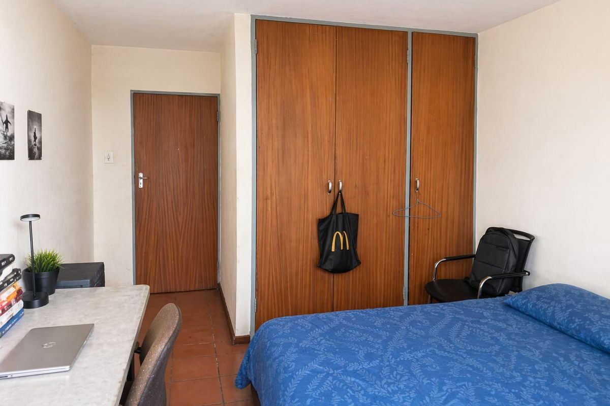 A functional bedroom featuring built-in wooden wardrobes, tiled flooring, and a standard internal door, offering a practical layout for living.