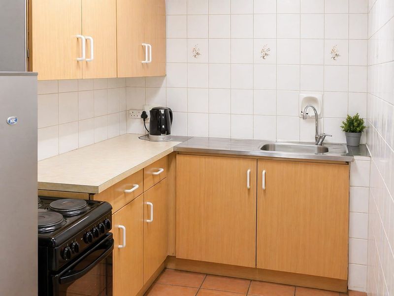 A compact kitchen featuring light wood-finish cabinetry, laminate countertops, a stainless steel sink, and tiled splashbacks.