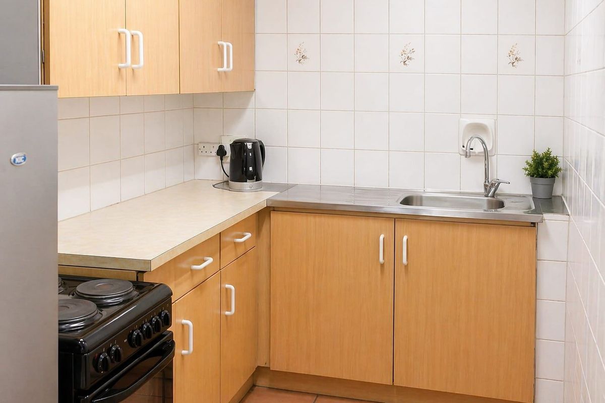 A compact kitchen featuring light wood-finish cabinetry, laminate countertops, a stainless steel sink, and tiled splashbacks.