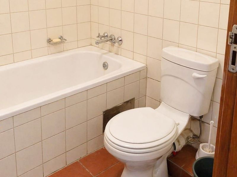 A functional bathroom featuring a built-in bathtub, ceramic wall and floor tiling, and a standard toilet suite.