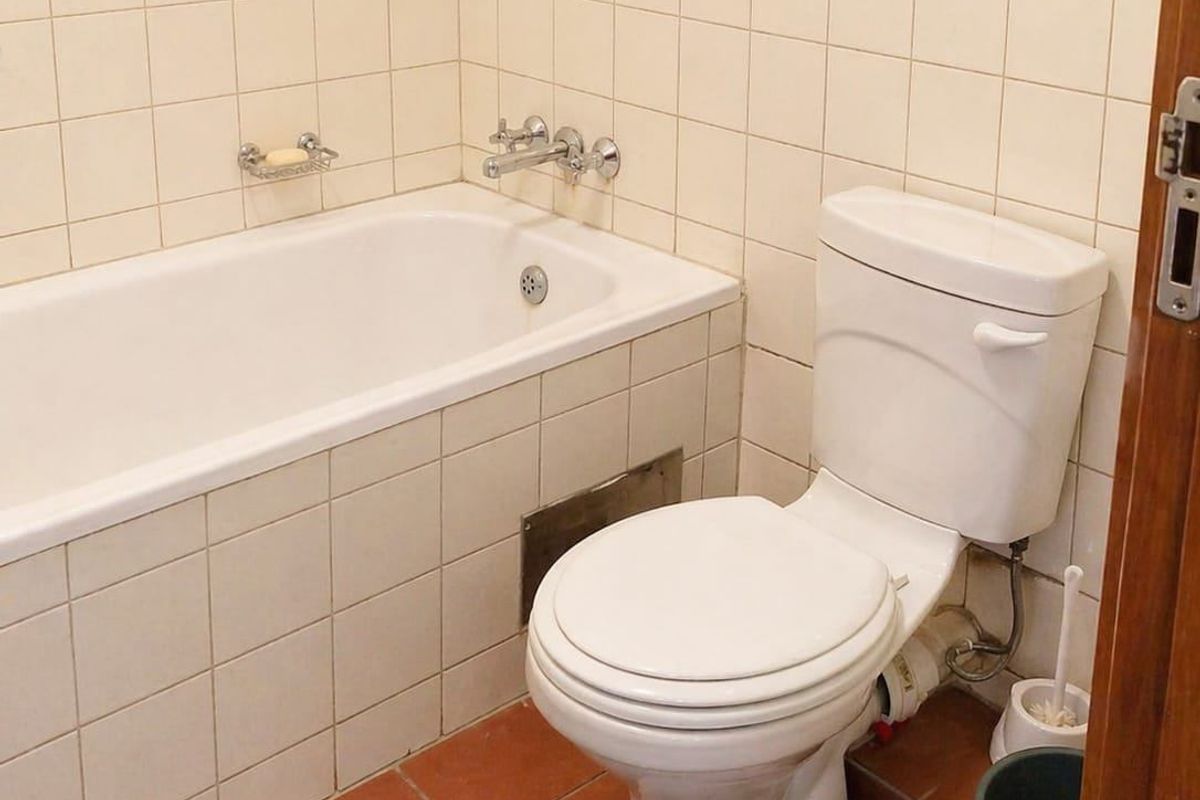 A functional bathroom featuring a built-in bathtub, ceramic wall and floor tiling, and a standard toilet suite.