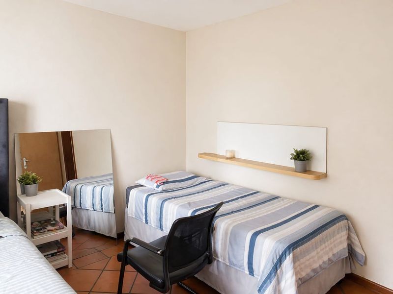 A functional bedroom featuring terracotta floor tiles and a wall-mounted floating shelf.