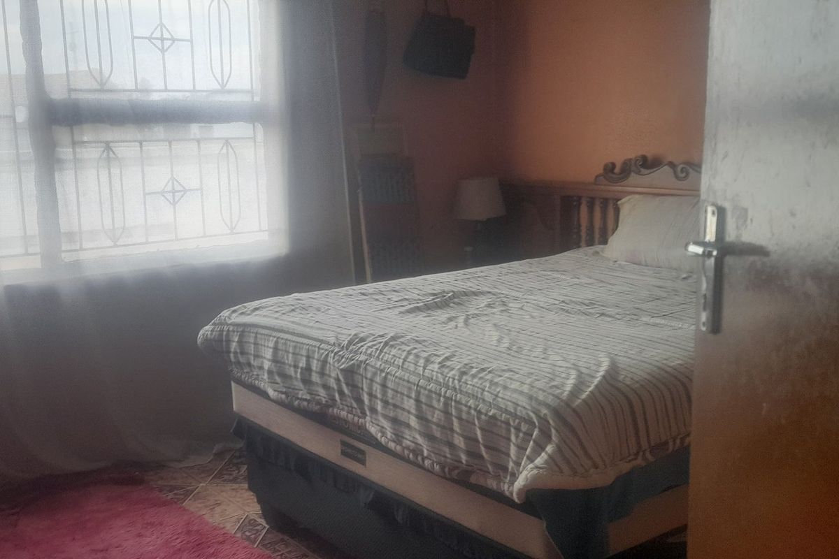A bedroom featuring tiled flooring and a window fitted with security bars, offering a functional space with natural light.