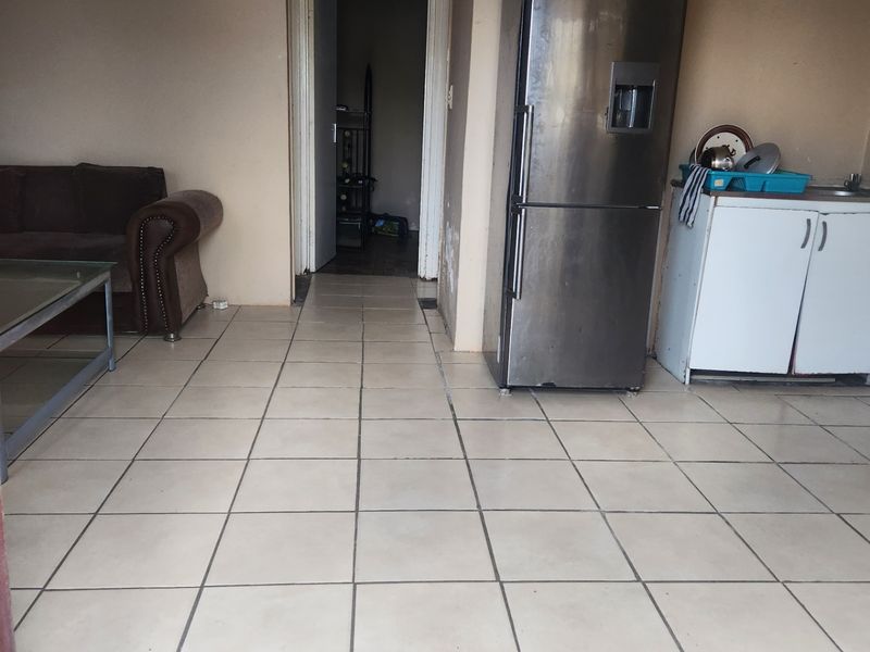 Open plan living area featuring tiled flooring and a compact kitchen corner with built-in cabinetry and sink.