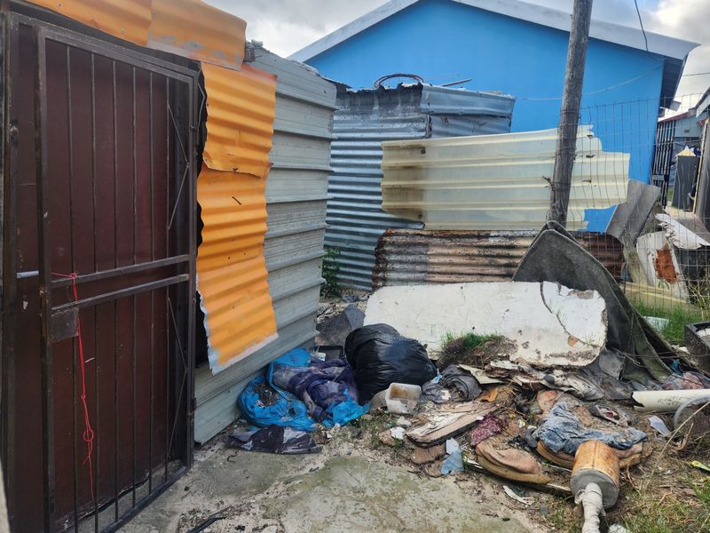 Rear exterior area featuring corrugated metal structures and a security gate, showing significant signs of wear and deterioration.