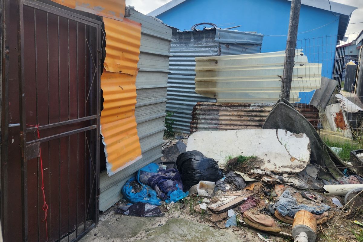 Rear exterior area featuring corrugated metal structures and a security gate, showing significant signs of wear and deterioration.