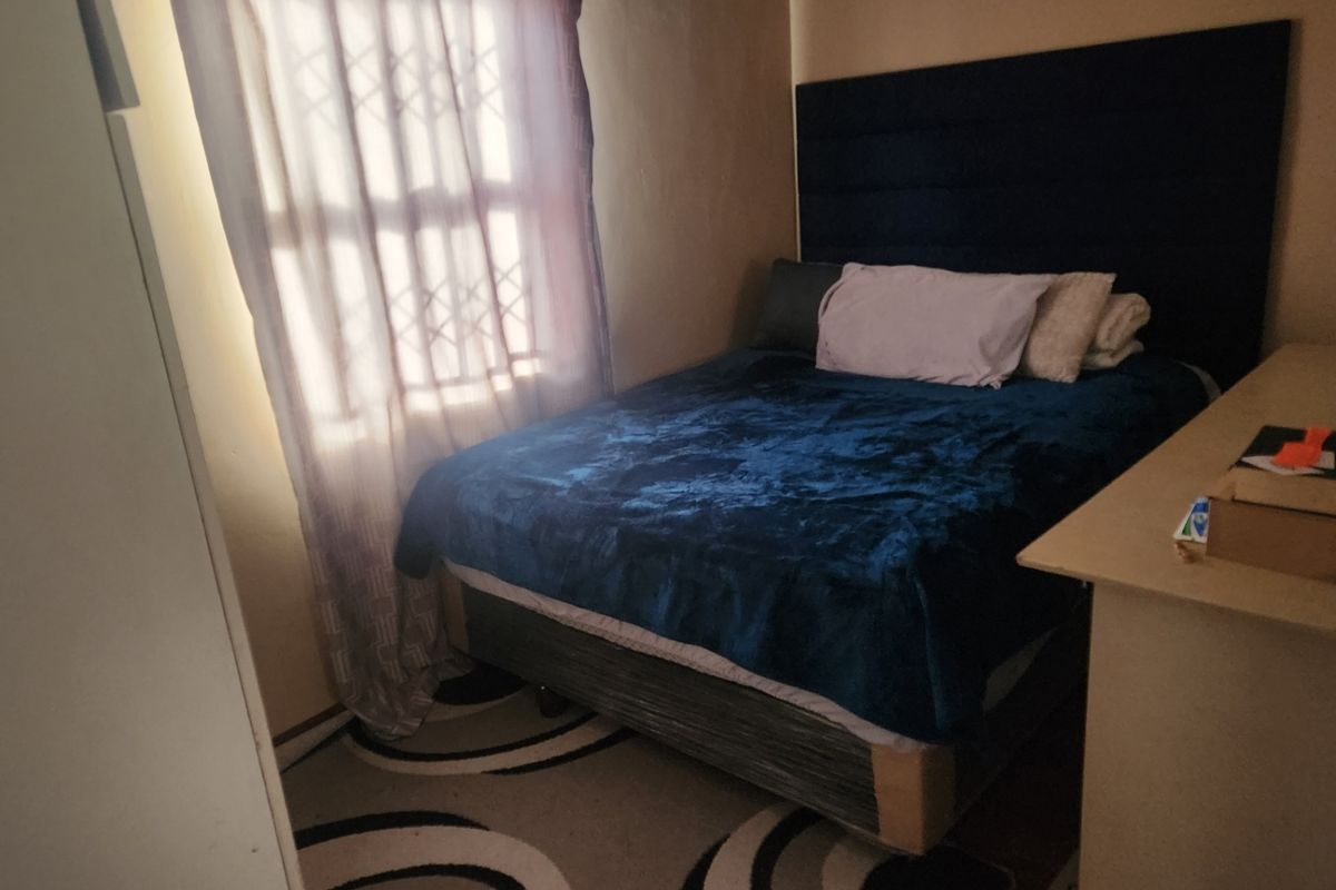 A compact bedroom featuring a window with a security gate and built-in storage space.