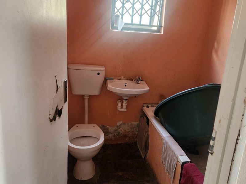 A compact bathroom featuring a toilet, wall-mounted basin, and bathtub, requiring significant cosmetic repairs and updates to the wall finishes and fixtures.